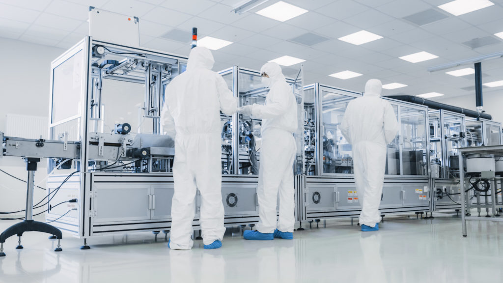 Medical manufacturing production workers wearing protective clothing and shoe covers.