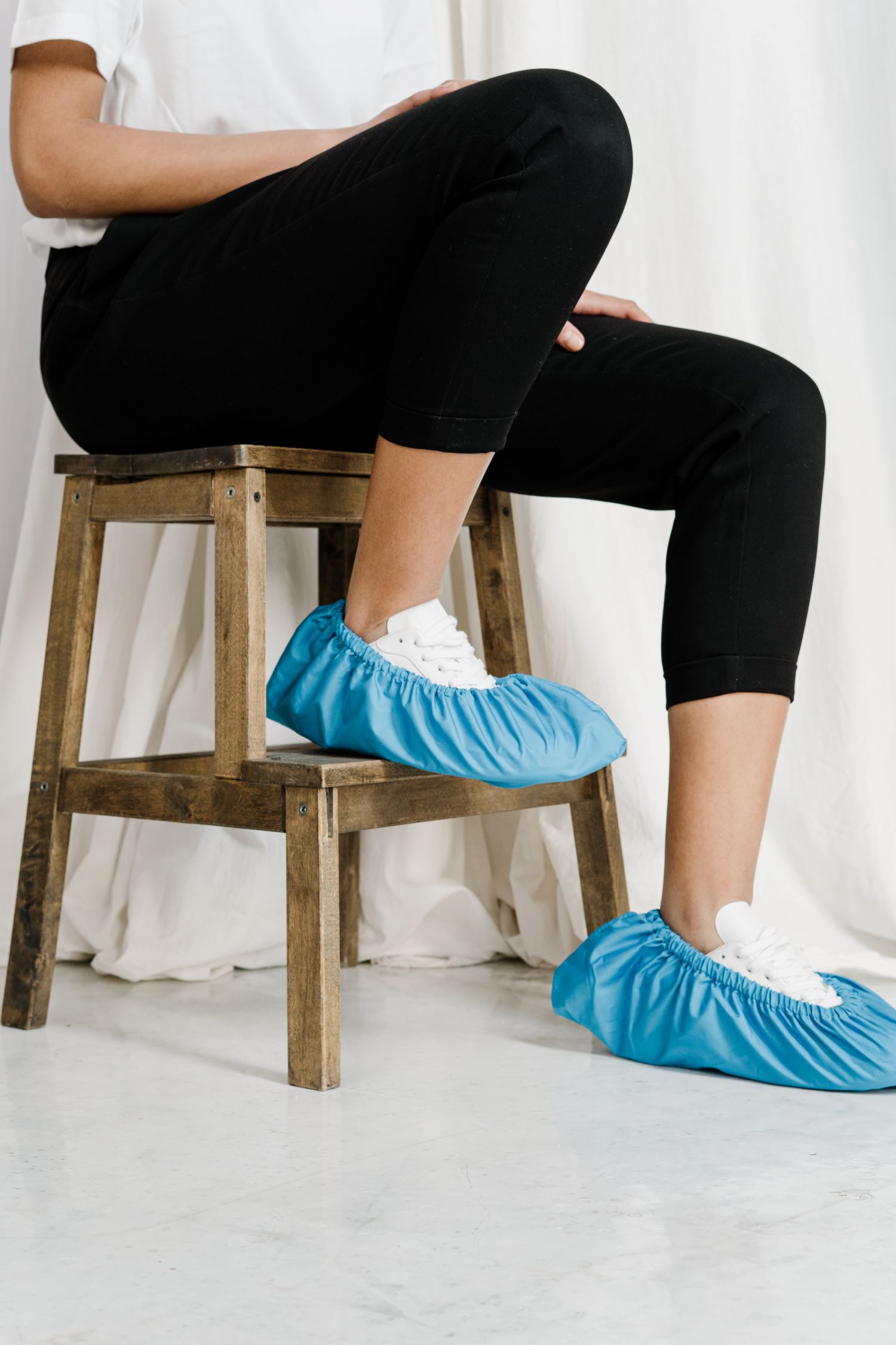Woman sitting on a stool with her white sneakers covered by shoe booties.