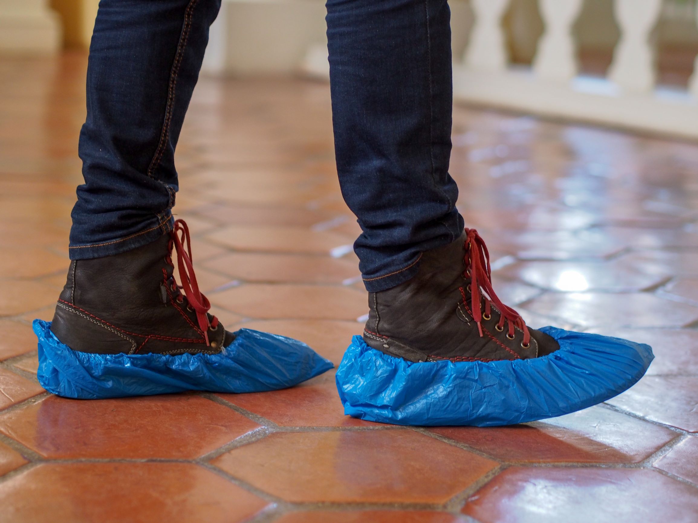 A person wearing fitted blue shoe covers on tile floor at home.