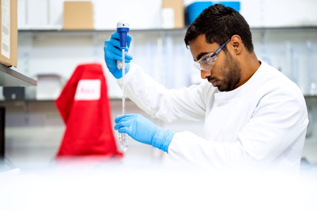 Scientist wearing PPE measuring out substances in a sanitary lab.