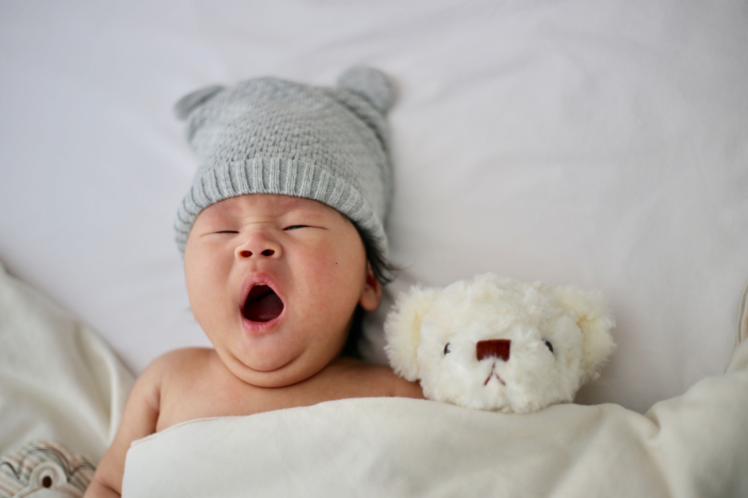Newborn child tucked into a bed with a small white stuffed bear.