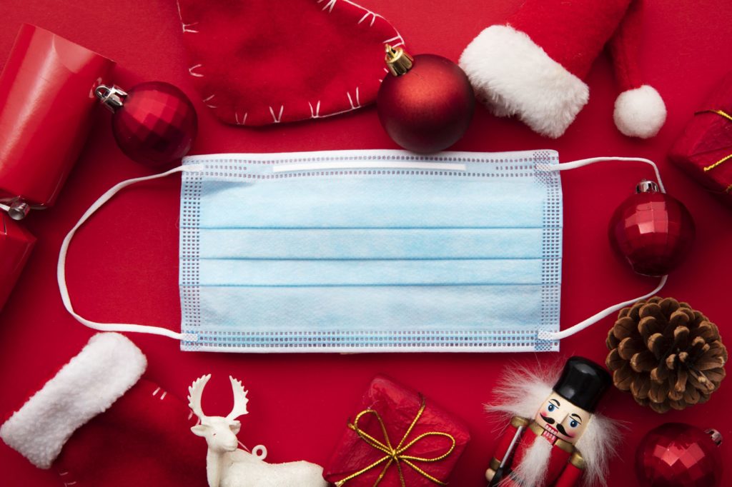 Protective mask on top of red background with scattered ornaments and Christmas decor.