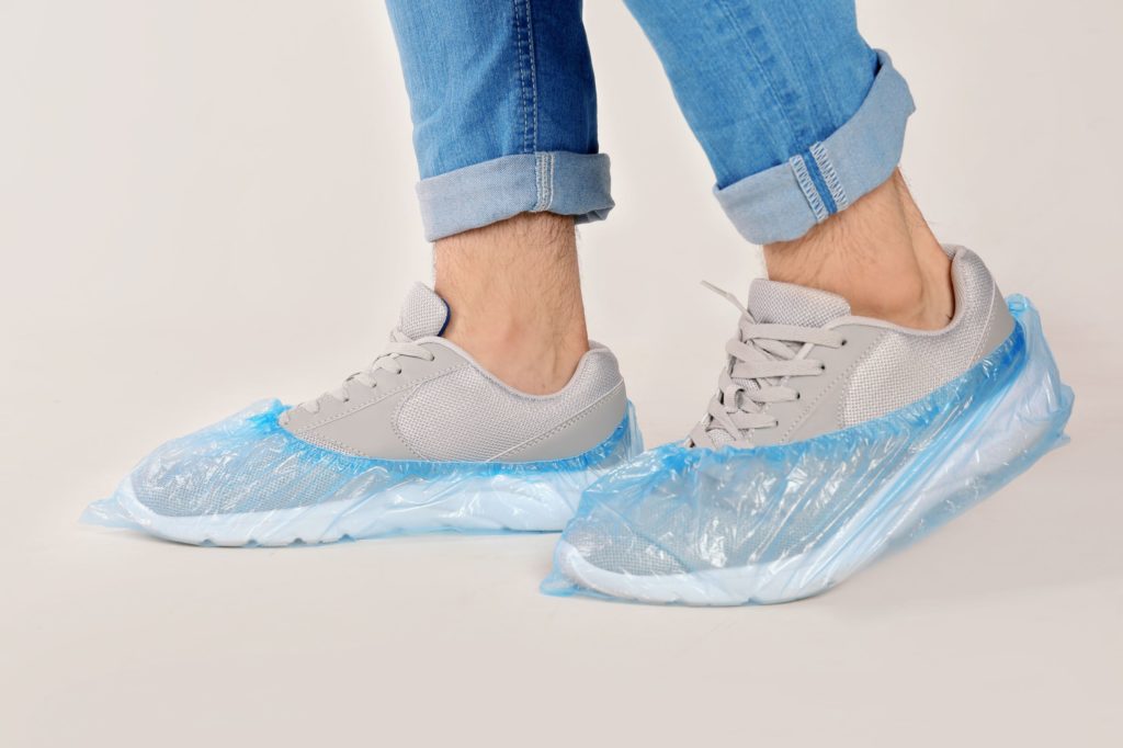 Person wearing disposable shoe covers over beige tennis shoes in a government building.
