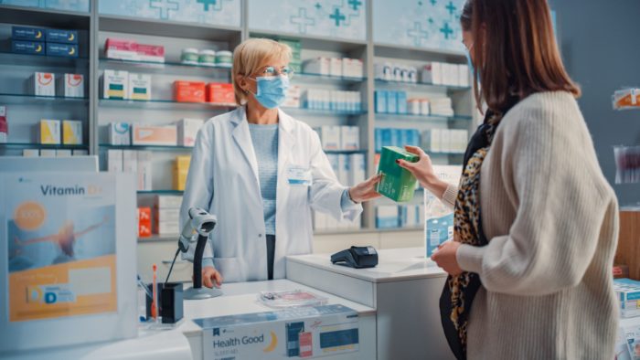 Pharmacist handing a customer her prescription wearing a medical mask.