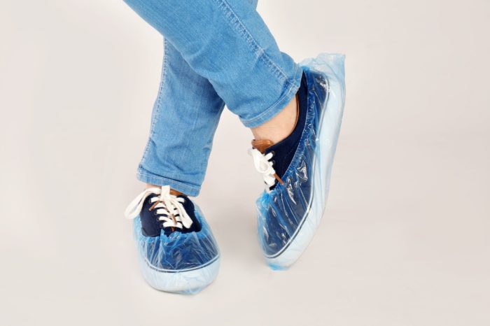 A person wearing navy and white sneakers with plastic shoe covers.