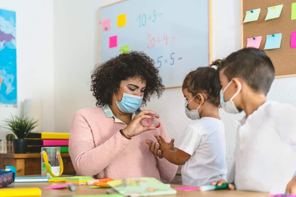 Elementary School teacher sanitizing students' hands for COVID-19..