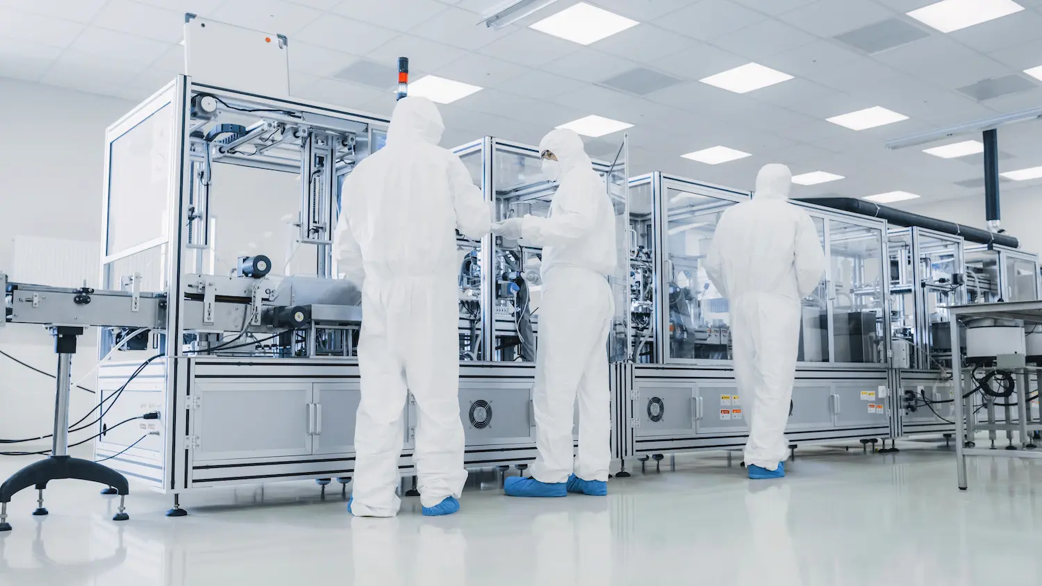 Medical manufacturing production workers wearing protective clothing and shoe covers.
