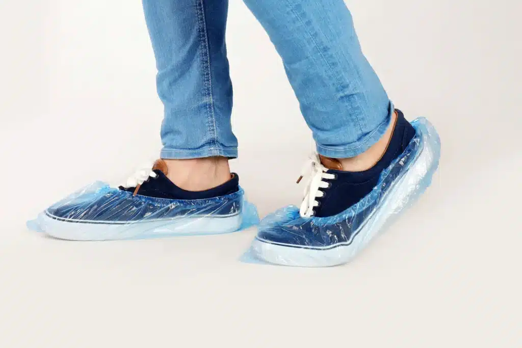 A person wearing navy and white sneakers with plastic shoe covers in the workplace.