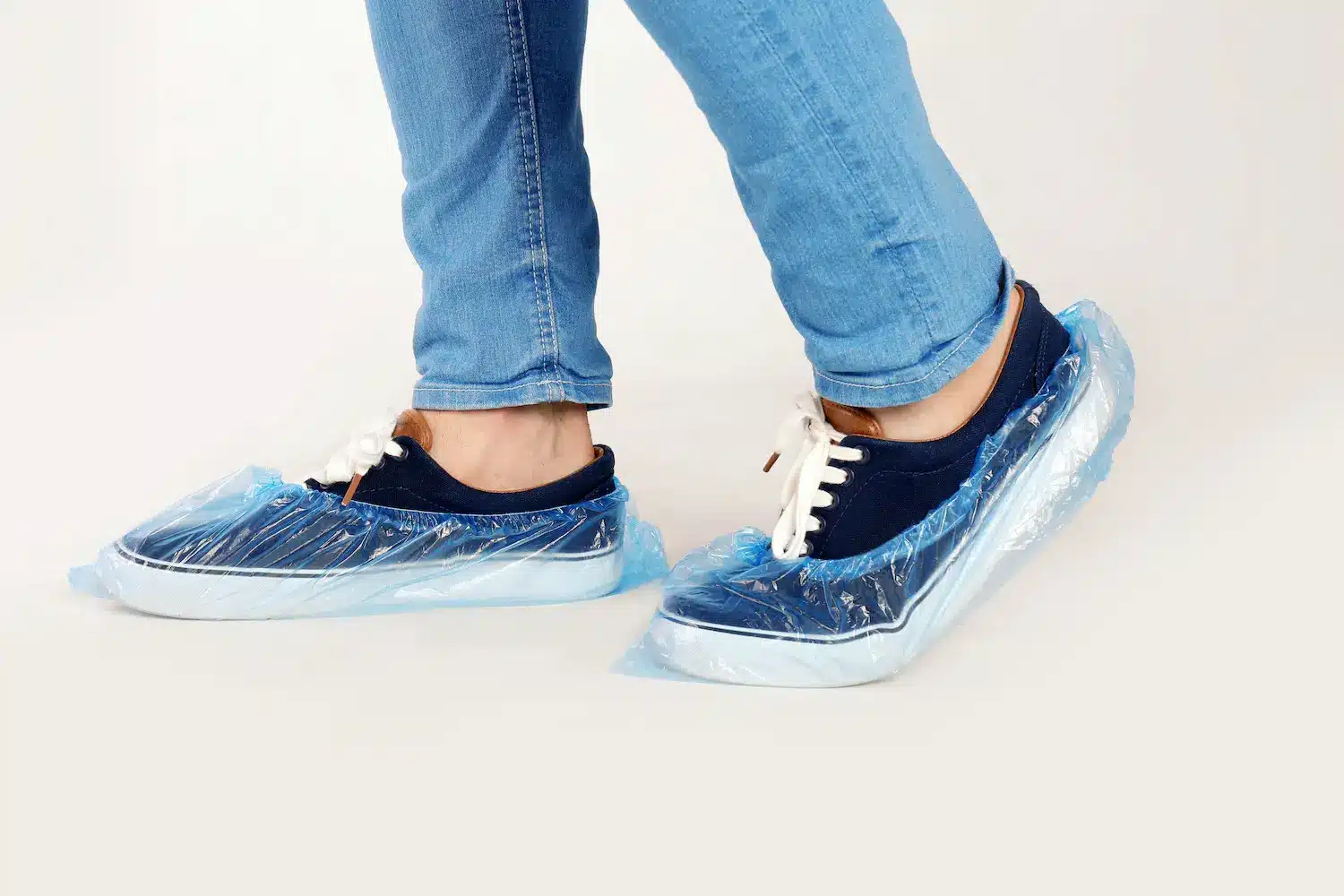 A person wearing navy and white sneakers with plastic shoe covers in the workplace.